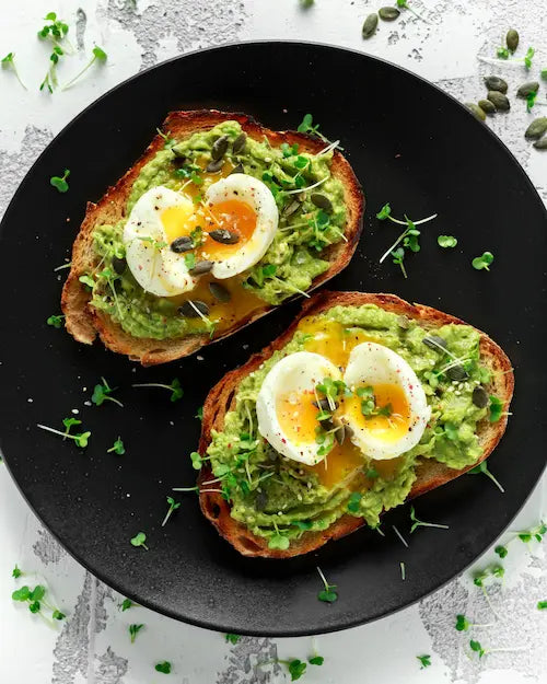 Avocado toast topped with soft eggs and sprouts, drizzled with extra virgin olive oil