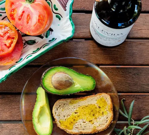Avocado and a slice of bread drizzled with extra virgin olive oil on a wooden table