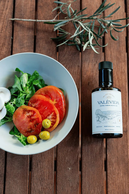 Bowl of salad with tomatoes and a bottle of Valevida olive oil on a wooden surface