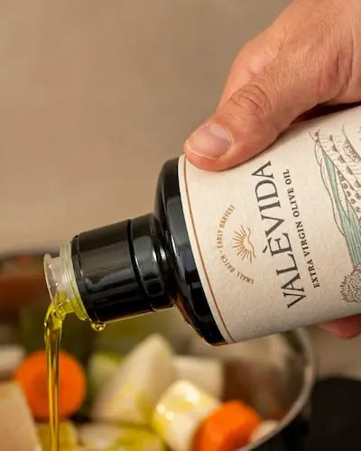 Valèvida extra virgin olive oil being poured over garlic and vegetables